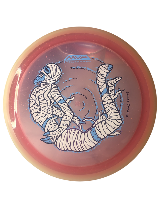 MVP Trail Proton Particle James Conrad Halloween Team Series 2026 – distance driver med mumiedesign, skimrande partiklar och självlysande kant.